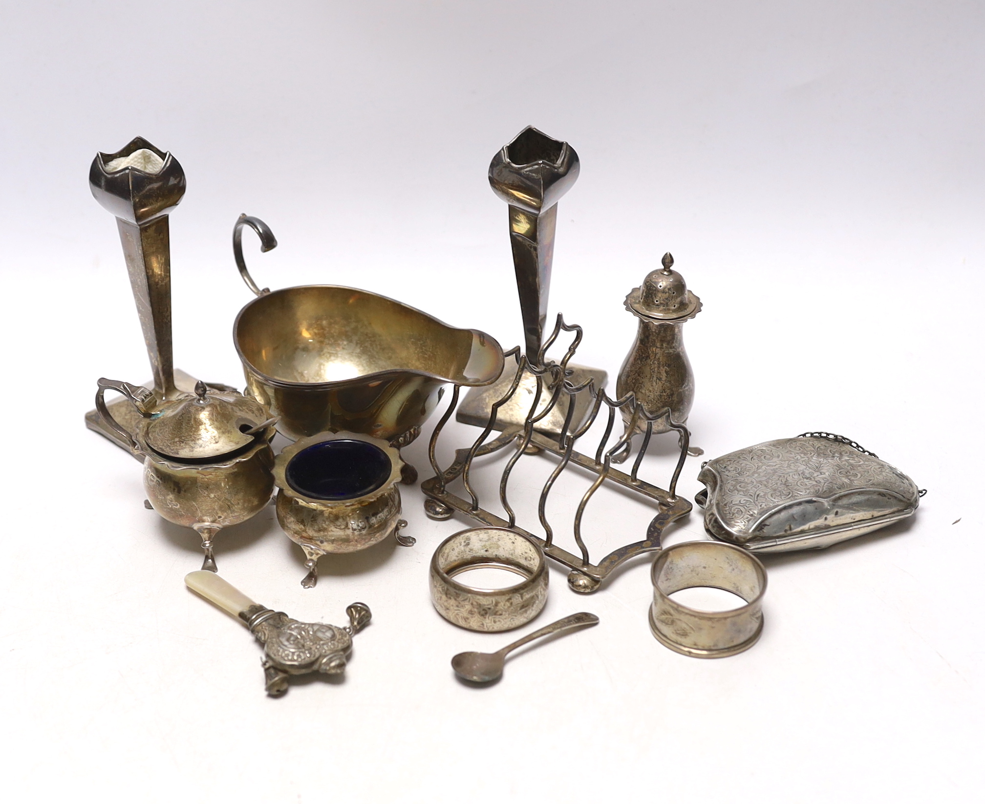 Sundry small silver including an Edwardian silver sauceboat, Birmingham, 1906, pair of spill vases (a.f.), a five bar toastrack, three condiments, a purse, two napkin rings and a child's rattle.